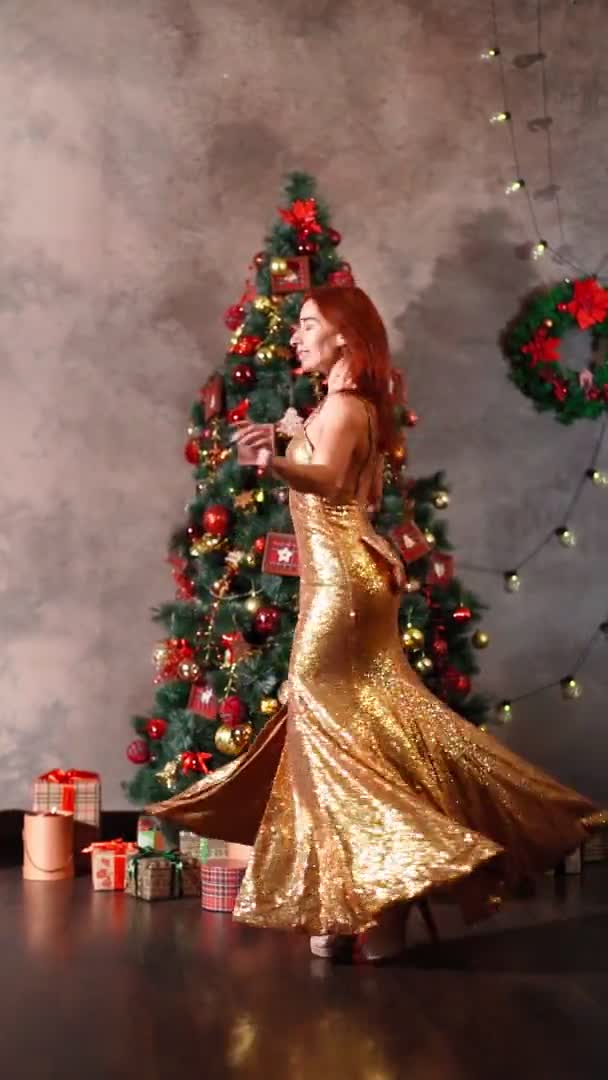 Mooie vrouw in gouden avondjurk spins en dansen in de buurt van kerstboom — Stockvideo
