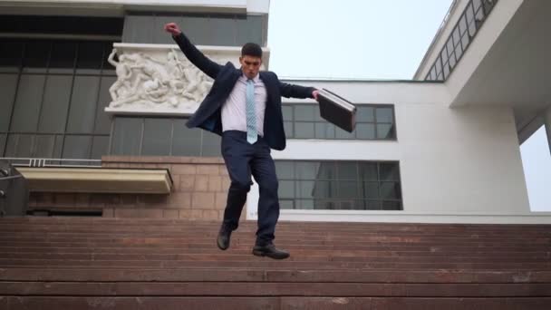 Щасливий успішний бізнесмен грайливо спускається сходами біля офісної будівлі . — стокове відео