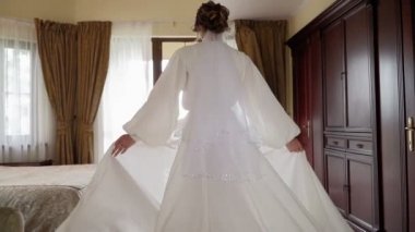 Güzel, gelişmekte olan beyaz cüppeli bir kadın yatak odasından balkona yürüyor..