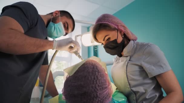 Zahnärztin Mit Schutzschild Und Gesichtsmaske Mit Hilfe Eines Männlichen Assistenten — Stockvideo