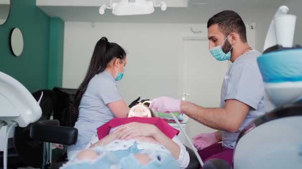 2人の医師歯科医医療マスクの女性と男性は 歯科事務所で患者の女の子に外科手術を行います 医療の概念 — ストック動画