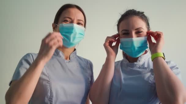 2人の美しい若い女性医師は顔の医療マスクと笑顔を削除します ヘルスケアと医療の概念 — ストック動画