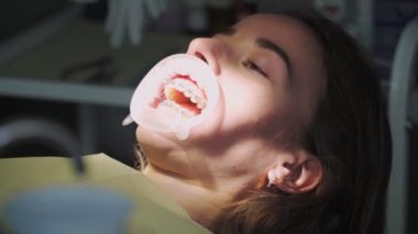 Diş Hekimliği Ofisinde Diş telleri ile Ağızda Retraktörü olan Komik Genç Hasta Bir Hastane Yatağında Yatıyor ve El Hareketi Gösteriyor. Sağlık ve Tıp Konsepti.