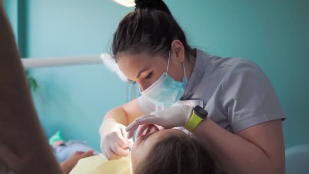 歯科医院の保護マスクの男と女の2人の医者は 患者の少女に奉仕します 歯医者だ 医療と医療の概念 閉じろ — ストック動画