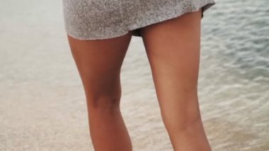 Gri kapüşonlu kazaklı yalnız kız kıyıdaki deniz boyunca gider. Ağır çekim. Yakın plan..