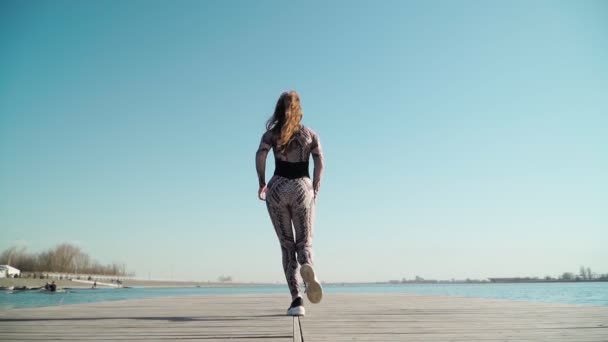 Athlète femme avec une belle silhouette court sur la jetée du lac. Mouvement lent. — Video