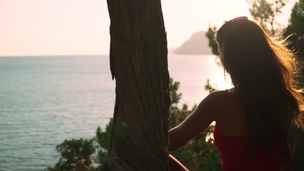 긴 머리를 가진 어린 운동 선수 소녀는 아름다운 바다와 해가질 무렵에 앉아 있다. 느린 동작 — 비디오