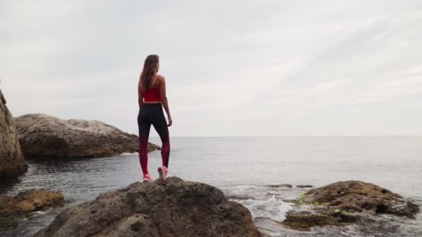 Auf einem Stein im Meer liegt ein sportliches Mädchen in Sportbekleidung. Zeitlupe. — Stockvideo