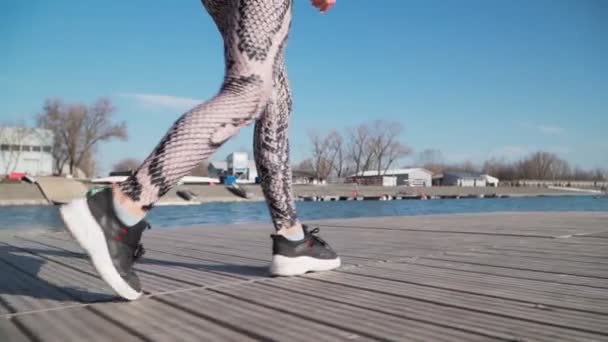 Aus nächster Nähe. Junge schlanke Frau in Sportbekleidung und schwarzen Turnschuhen steht auf der Seebrücke — Stockvideo