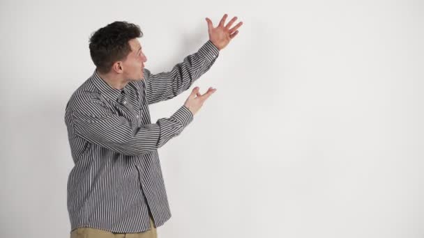 En ung man med kaukasiska utseende i en skjorta på en vit bakgrund visar känslan av beundran — Stockvideo