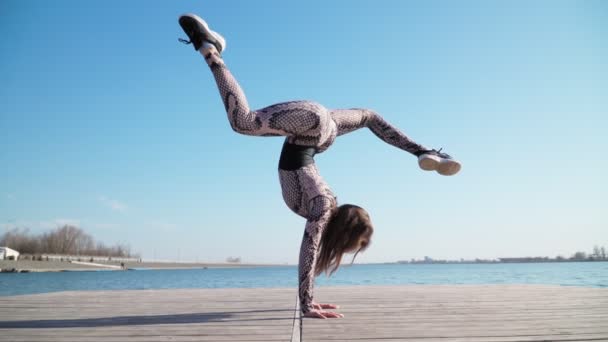 Atlet muda pesenam wanita melakukan handstand, di ponton dekat danau biru. Gerakan lambat. — Stok Video