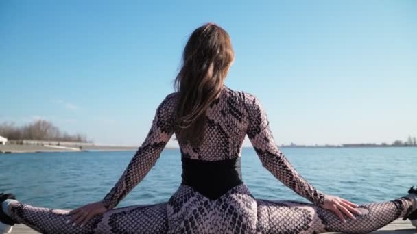 Athletische schlanke junge Mädchen sitzt in Splits auf dem Hintergrund schönen blauen See. Yoga-Kurse im Freien — Stockvideo