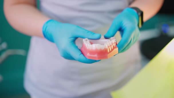 Женщина-дантист держит челюсть в руках и говорит с пациентом в стоматологической клинике — стоковое видео