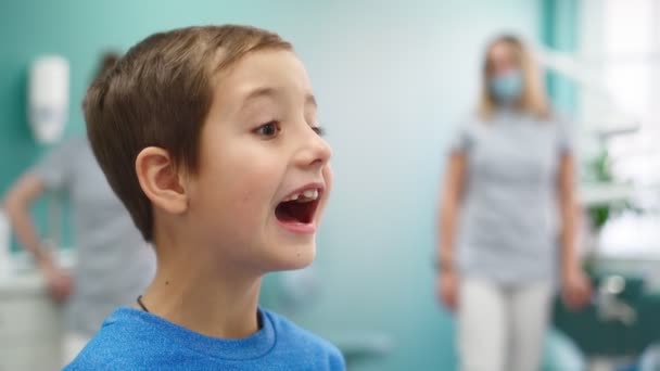 웃긴 소년이 치과 병원에서 손상 된 아기의 치아를 거울 속에 담고 있다 — 비디오