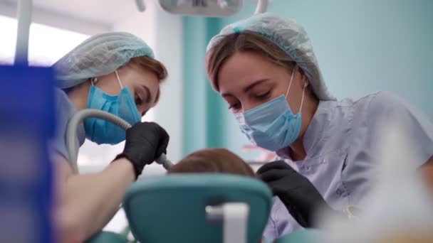 Deux femmes médecins en masque médical dans une clinique dentaire, servir le patient petit garçon — Video