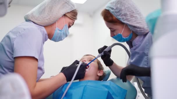 Dos doctores en gorra médica en la clínica dental, sirven al niño pequeño paciente — Vídeos de Stock