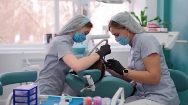 Diş Kliniğinde Tıbbi Maskeli İki Kadın Doktor Hasta Çocuğa Hizmet Ediyor.