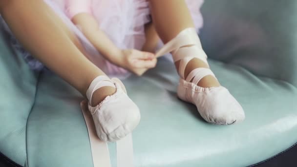 Linda niña en tutú rosa sentada en silla azul y atando zapatos de ballet. De cerca. pequeña bailarina — Vídeos de Stock