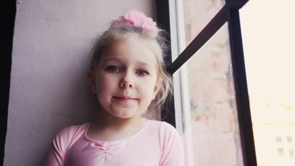 ピンクのドレスにかわいい赤ちゃんの女の子の肖像画と頭の上に弓。窓の近くに立って悲しい — ストック動画