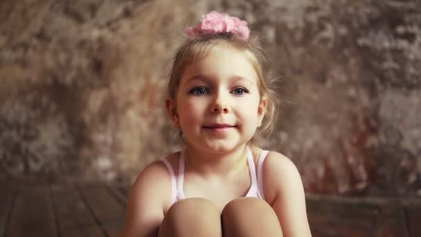 Smutná malá roztomilá holčička s luky na hlavě sedí na podlaze se zkříženýma nohama. — Stock video