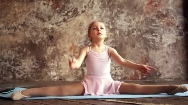 Küçük kız jimnastikçi, ikiye ayrılıp ısınıyor. Çocuk sporları. Sarışın Bebek. 