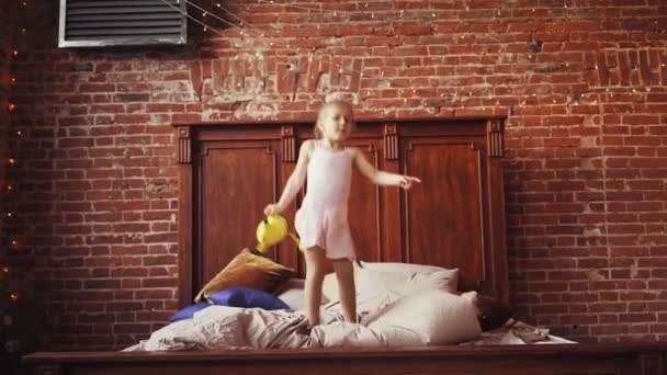 Söt liten flicka blondin Med en mjuk leksak i händerna hoppar på sängen. Barndom. Lycka och glädje — Stockvideo