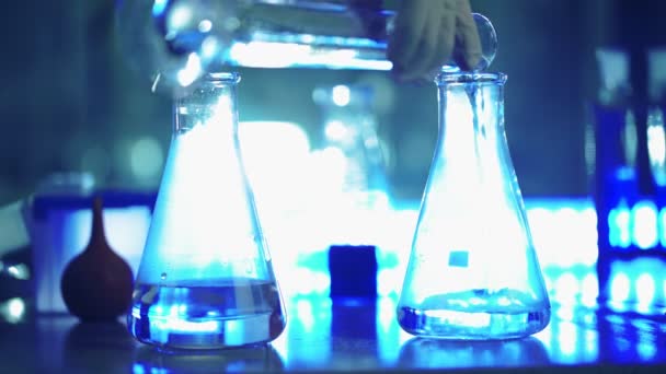 Wetenschapper in laboratorium doet chemisch experiment met vloeistof in kolven — Stockvideo