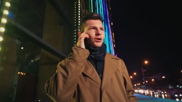 Irritado homem falando no telefone celular fora brilhando shopping center à noite — Vídeo de Stock