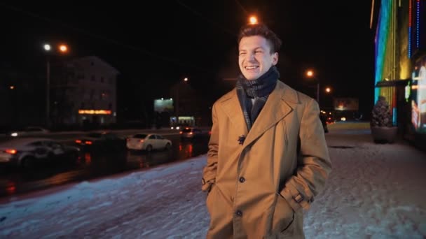 Mutlu gülümseyen adam kış gecesinde otoyol kenarındaki sokak kenti boyunca yürür.. — Stok video