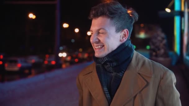 Feliz homem sorridente caminha na noite de inverno ao longo da cidade de rua perto da rodovia. — Vídeo de Stock