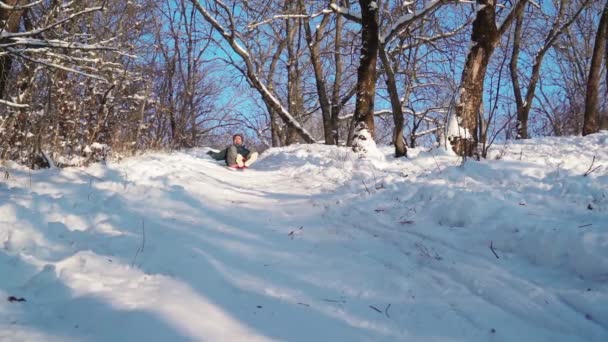 Happy Man jezdí na saních ze Sněžného kopce. Guy se baví v zimním lese. — Stock video