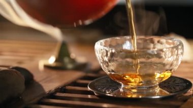 Çay, cam arka plana döküldü. Duman kokulu çubuklar, sıcak ışıkla aydınlatılıyor.