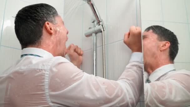 Triste homem de camisa e gravata fica no banheiro sob chuveiro e banheiras em roupas — Vídeo de Stock