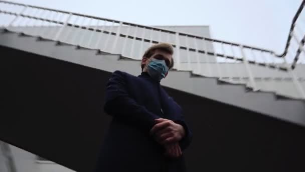 Szomorú üzletember orvosi maszkban az arcán megáll és lenéz a hóesés alatt — Stock videók
