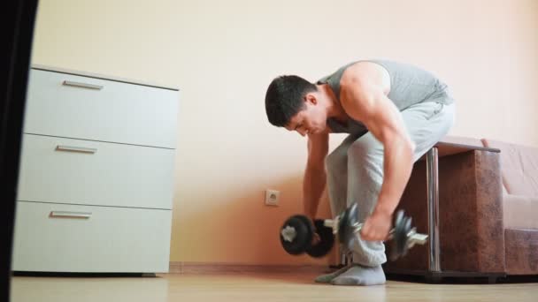 Muskulöser, athletischer Mann beim Training mit Kurzhanteln zu Hause auf dem Bett angelehnt. — Stockvideo
