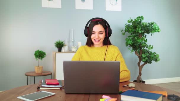 헤드폰을 끼고 있는 행복 한 여성 학생 이 집에서 웹캠 채팅으로 학습을 하고 있습니다.. — 비디오