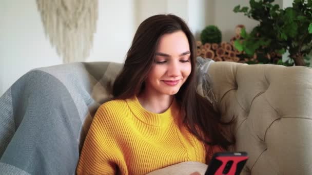 Kvinna ler Hold Smartphone Titta på sociala medier berättelser Video Sitt på soffan — Stockvideo