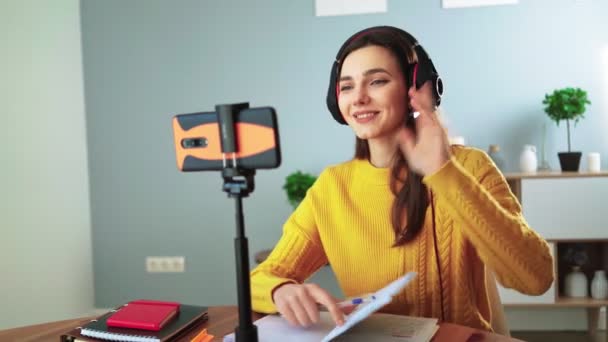 Lykkelig ung lærer i hovedtelefoner kommunikerer via videoopkald ved hjælp af mobiltelefon. – Stock-video