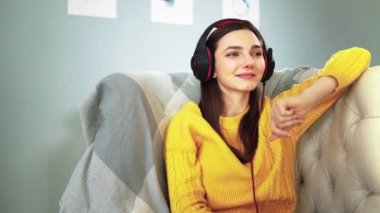 Kulaklıklı, gözleri kapalı bir kız rahat koltukta dinleniyor ve müzik dinliyor.