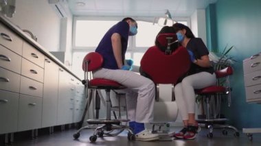 Diş hekimleri kadın ve erkek doktor maskeli hastalara diş sağlığı kliniğinde hizmet veriyor.