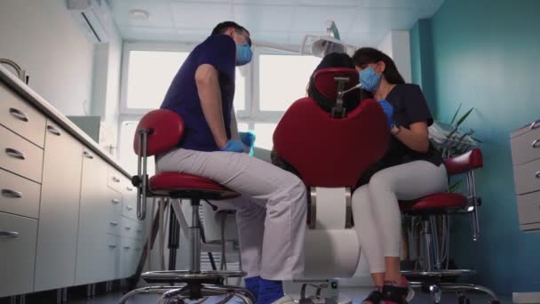 Médicos dentistas mulher e homem em máscaras médicas servem paciente na clínica odontológica — Vídeo de Stock