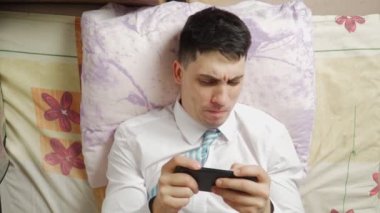 Komik adam telefonda oyun oynuyor ve evdeki kanepede yatarken kazanıyor..