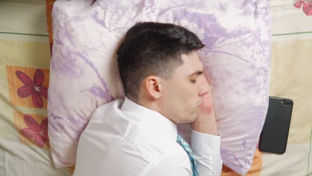 Hombre agotado en ropa de oficina dormir en la cama después del trabajo y se despierta anillo de teléfono — Vídeo de stock