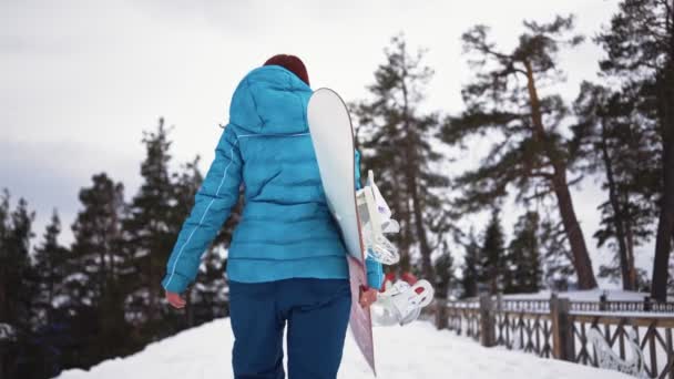 Kar altında elinde snowboard 'la dolaşan bir kız. Kışın açık hava aktiviteleri — Stok video