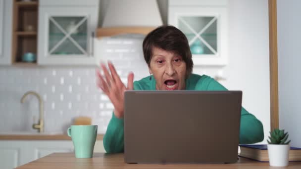 Feliz anciana comunicándose por videollamada usando portátil en casa en la cocina — Vídeos de Stock