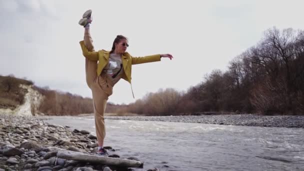 Flicka gör sprickor på bakgrund berg flod och stenar. Kvinna utövar yoga — Stockvideo