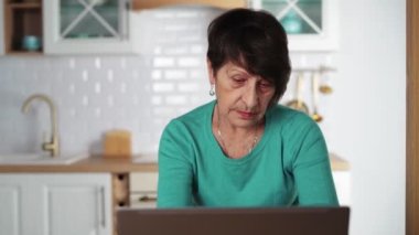 Laptop 'ta uzaktan çalışan yaşlı bir kadın dizüstü bilgisayarda klavye kullanıyor.
