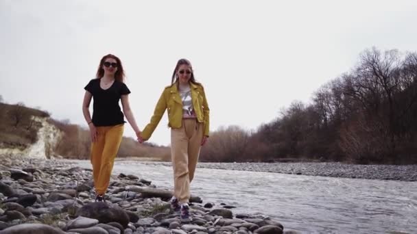 Dwie lesbijki trzymają się za ręce i spacerują górską rzeką. Pojęcie wolności LGBT — Wideo stockowe