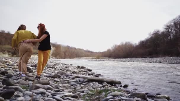 Dos chicas felices se están divirtiendo en la orilla del río. Las mujeres alegres juegan divertido — Vídeos de Stock
