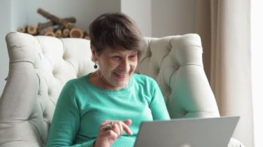  Happy elderly woman communicating by video call using laptop at home